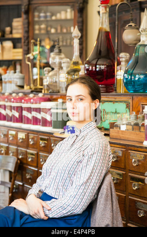 Giovane donna assistente vendite seduto in farmacia vittoriano/ farmacia, a Blists Hill Città Vittoriano museum, England Regno Unito Foto Stock