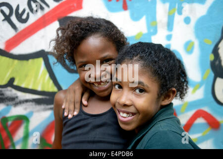 Due ragazze sorridenti che abbraccia ogni altro di fronte a un graffiti spruzzati in parete, baraccopoli, Mangueirinha favela, Duque de Caxias Foto Stock