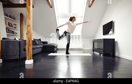 Lunghezza completa immagine di montare la giovane donna a praticare yoga a casa. Sano giovane donna che esercitano nel soggiorno. Modello caucasico. Foto Stock