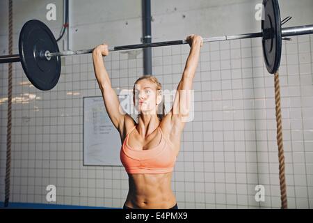 Bella forte giovane donna con barbell e piastre di peso overhead. Montare il giovane atleta femminile di sollevamento pesi pesanti. Caucasian Foto Stock