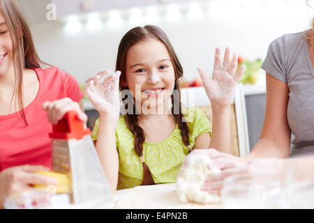 Ritratto di felice ragazza mostrando il suo palme infarinata con la madre e la sorella la cottura nelle vicinanze Foto Stock