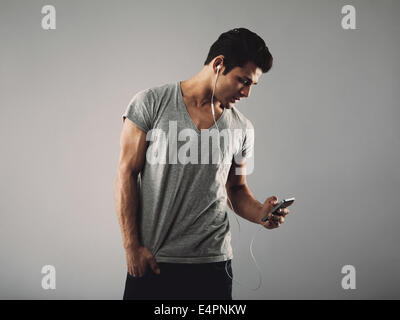 Bel giovane in t-shirt casual ascoltando la musica sul telefono cellulare. Ispanico modello maschile che indossa gli auricolari e ascolto di musica Foto Stock