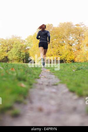 Vista posteriore immagine della giovane donna jogging in un parco in un giorno d'estate. Montare e sano atleta femminile esercizio in esecuzione nel parco. Foto Stock