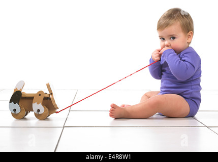 Baby girl (12 mesi) mordere stringa di tirare lungo il giocattolo per cane Foto Stock