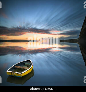 Singolo battello floating n. acqua durante il sunrise oltre oceano con faro e parete del porto Foto Stock