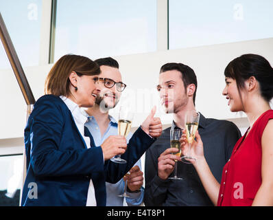 Imprenditrice matura la tostatura del gruppo di giovani uomini di affari con bicchieri di champagne, Germania Foto Stock