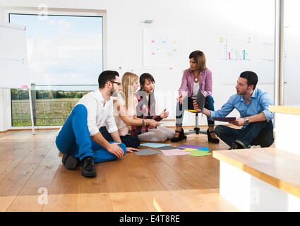 Coppia imprenditrice incontro con un gruppo di giovani imprenditori, seduto sul pavimento in discussione, Germania Foto Stock