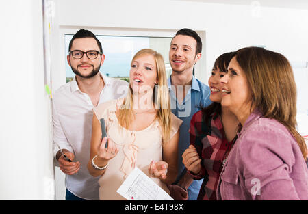 Coppia imprenditrice incontro con un gruppo di giovani imprenditori, guardando la scheda bianca e sorridente, Germania Foto Stock