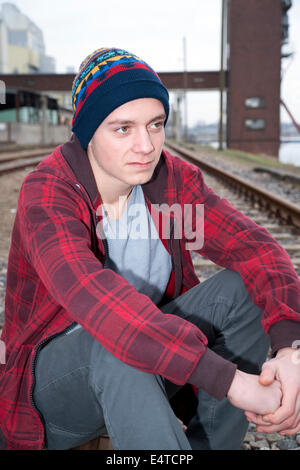 Close-up ritratto di ragazzo adolescente seduto sui binari della ferrovia nei pressi del porto, Germania Foto Stock