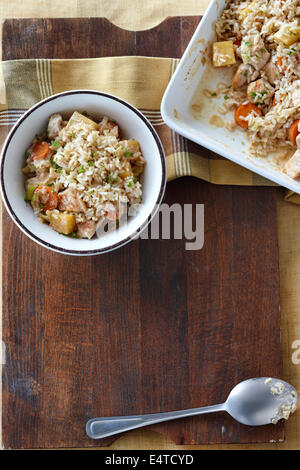 La Turchia e riso bianco casseruola con pastinaca, carote e prezzemolo fresco su un tagliere di legno su un piano di un tavolo Foto Stock