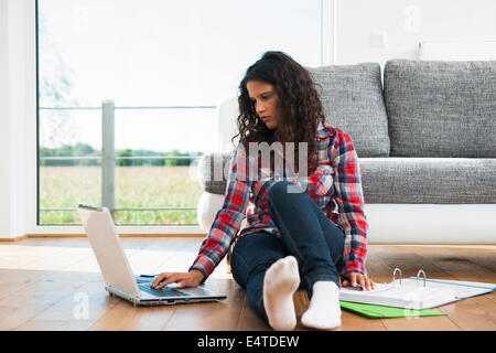 Ragazza seduta sul pavimento accanto al divano, utilizzando il computer portatile, Germania Foto Stock