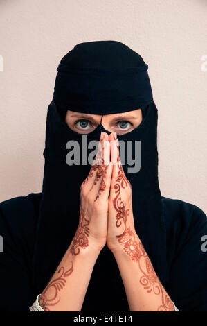 Ritratto di donna in nero musulmano hijab e abiti musulmani, mani pregando e verniciati con colore henné in stile arabo Foto Stock