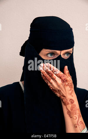 Ritratto di donna in nero musulmano hijab e abiti musulmani, mano a copertura della bocca, delle mani dipinte con henna in stile arabo Foto Stock