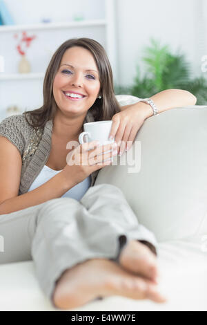 Donna felice di bere una tazza sul divano Foto Stock