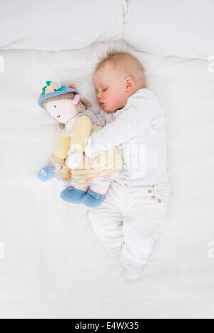 Baby dormendo mentre abbracciando una bambola di peluche Foto Stock