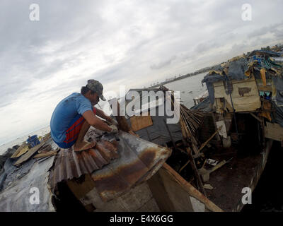 Manila, Filippine. 17 Luglio, 2014. Un uomo che ripara il tetto della sua casa dopo che è stato danneggiato dal tifone Rammasun presso una delle baraccopoli di Manila, Filippine, il 17 luglio 2014. Il tributo di morte pagato typhoon Rammasun è salito a 38, il locale disastro Agency ha detto giovedì. Il disastro nazionale di riduzione dei rischi e di Consiglio di Gestione (NDRRMC) detto il tifone anche lasciato 10 feriti mentre altri otto sono state dichiarate mancanti. Credito: Rouelle Umali/Xinhua/Alamy Live News Foto Stock