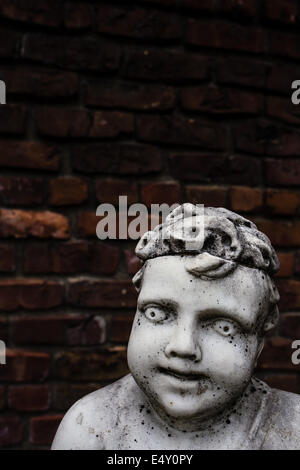 Un vecchio creepy vintage giardino in marmo statua di un cherubino o ragazzo contro e il vecchio muro di mattoni. Copia spazio sopra. Foto Stock