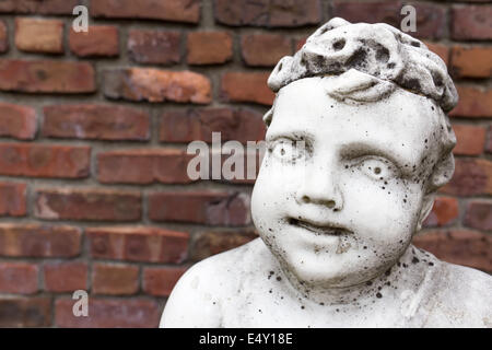 Una vecchia statua in marmo bianco di un cherubino ragazzo contro un muro del giardino con spazio di copia. Foto Stock