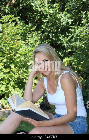 Bella donna sorridente lettura in giardino Foto Stock