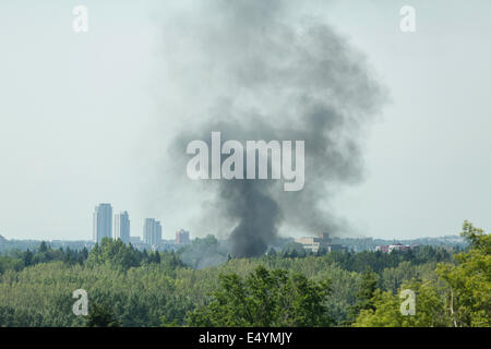 Un incendio in garage manda in aria una folta pennacchio di fumo nero di fronte allo skyline di Calgary, visto dall'alto degli alberi a pochi chilometri di distanza. Foto Stock