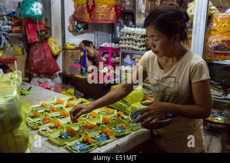 Bali, Indonesia. Donna facendo offerte (Canang) per vendere nelle prime ore del mattino per mercato di Jimbaran. Foto Stock