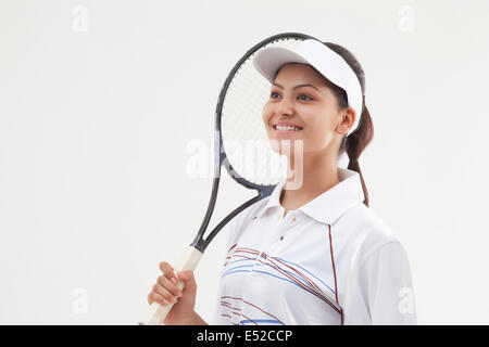 Felice giovane donna holding racchetta da tennis mentre guarda lontano isolate su uno sfondo grigio Foto Stock