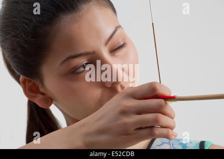 Close-up di giovani femmine archer praticare il tiro con l'arco contro uno sfondo grigio Foto Stock