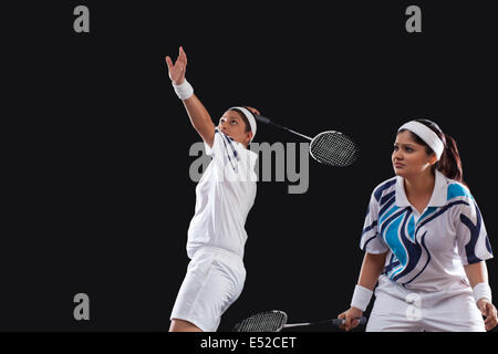 Giovani femmine i giocatori che giocano raddoppia badminton isolate su sfondo nero Foto Stock