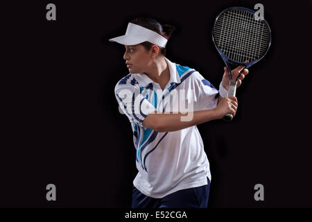 Giovane donna indiana giocando a tennis su sfondo nero Foto Stock