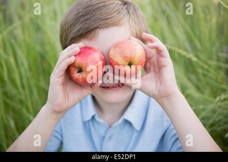 Un ragazzo tenendo due red scuoiati mele oltre i suoi occhi. Foto Stock