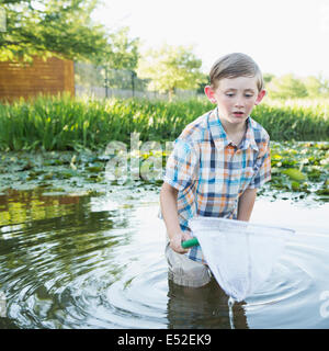 Un giovane ragazzo accanto alla coscia profondo in acqua con una rete da pesca. Foto Stock