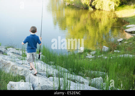 Un ragazzo con la sua canna da pesca sulla riva di un lago o di un fiume. Foto Stock