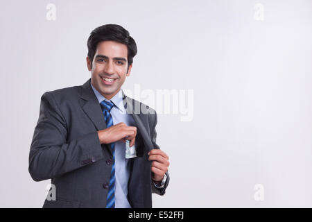 Ritratto di imprenditore sorridente mantenendo i soldi in tasca su sfondo grigio Foto Stock