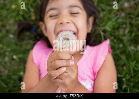 Una ragazza distesa sul terreno, tenendo un tarassaco seedhead orologio. Foto Stock