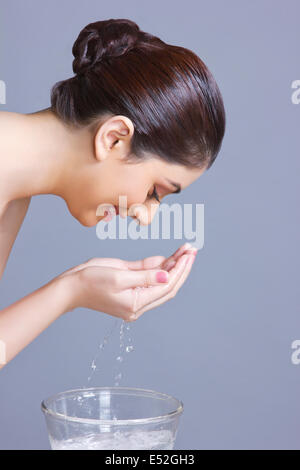 Colpo di Profilo di donna faccia il lavaggio con acqua contro sfondo blu Foto Stock