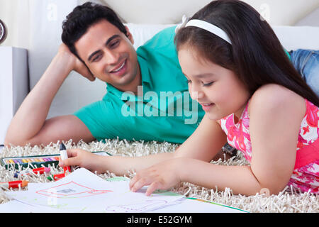 Bambina disegno mentre giacenti da padre sul tappeto a casa Foto Stock