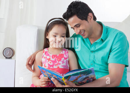 Felice padre e figlia alla lettura della storia libro sul divano di casa Foto Stock