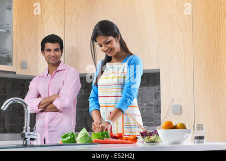 Uomo che guarda la donna come tagliare le verdure in cucina Foto Stock