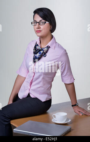Ritratto di fiducioso imprenditrice seduta sulla scrivania in ufficio Foto Stock