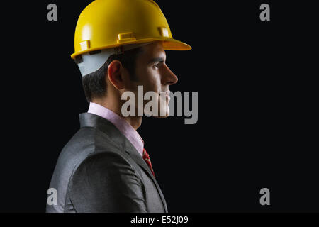 Vista laterale del giovane imprenditore indossando hardhat su sfondo nero Foto Stock