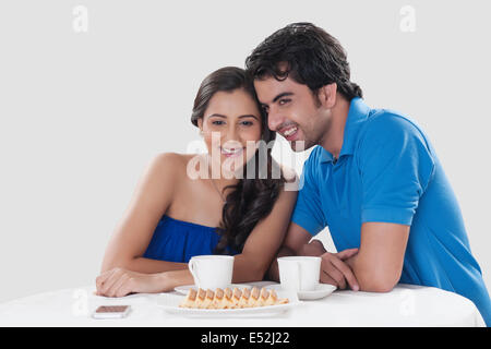 Felice coppia giovane che guarda lontano mentre avente caffè contro sopra lo sfondo Foto Stock