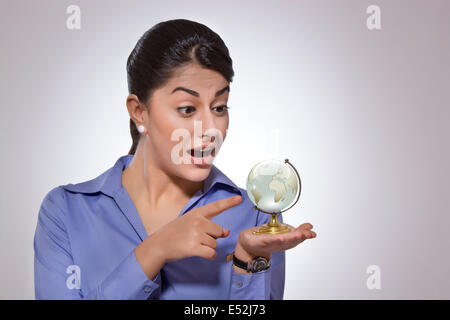 Sorpreso imprenditrice puntando al globo di cristallo su sfondo grigio Foto Stock