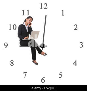 Imprenditrice utilizzando computer portatile mentre è seduto sulla mano di clock che rappresentano il fine di lavorare contro uno sfondo bianco Foto Stock