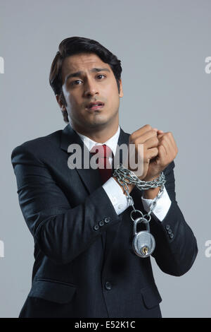 Ritratto di triste imprenditore legato in catena contro uno sfondo grigio Foto Stock