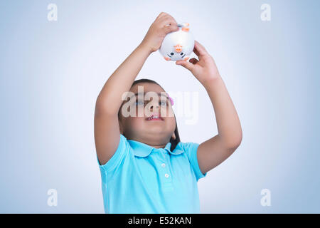 Ragazza in cerca di monete nel salvadanaio contro sfondo blu Foto Stock