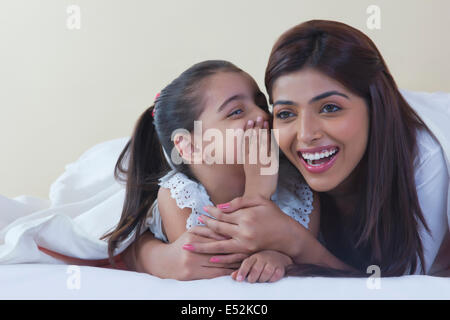 Ragazza whispering in madre l orecchio sul letto Foto Stock