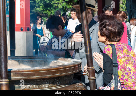 Luce buddisti di incenso e di pregare presso il tempio Sensoji di Asakusa quartiere di Tokyo, Giappone. Foto Stock