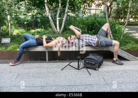 Giovane turista giovane prendendo una pausa per controllare le loro foto su una linea alta una panchina nel parco ombreggiato da lussureggiante fogliame estate Manhattan Foto Stock