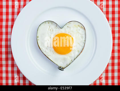 Uovo fritto a forma di cuore sulla tovaglia vintage. La prima colazione per una persona amata Foto Stock