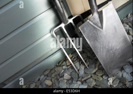 Forcella di giardino e vanga appoggiata contro un capannone verniciato Foto Stock